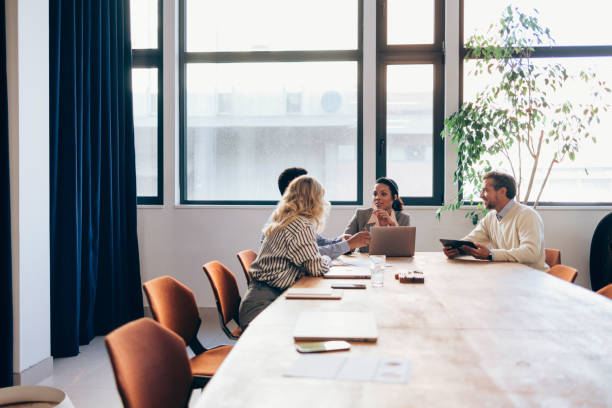 Diverse group of professionals engage in discussion in a well-lit meeting room with modern furnishings and a calm atmosphere.